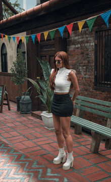 a woman wearing a white crop top and black skirt stands in front of a green bench