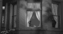 a black and white photo of a man looking out of a window