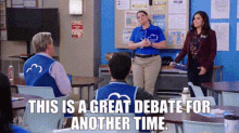 a group of people are sitting at tables in a classroom while a woman stands in front of them .