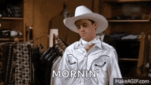 a man wearing a cowboy hat and bow tie is standing in a closet and saying morning .