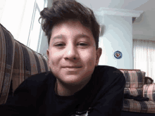 a young boy is sitting on a couch in a living room and smiling at the camera .