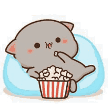 a cartoon cat is eating popcorn while laying on a blue pillow .