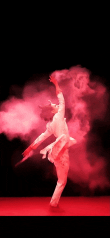 a man in a white suit is dancing in front of red smoke .