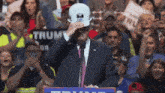 a man in a suit and tie is wearing a hard hat while standing at a podium in front of a crowd .