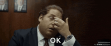 a man in a suit and tie is rubbing his eyes and the word ok is visible