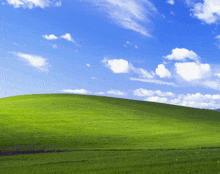 a green hill with a blue sky and white clouds in the background