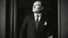 a man in a suit and tie is standing in front of a curtain and looking up .