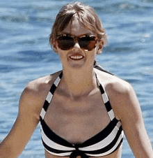 a woman in a black and white striped bikini and sunglasses is smiling in the water .