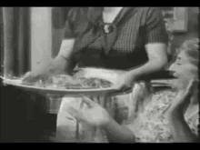 a woman is holding a tray of food and talking to another woman in a black and white photo .