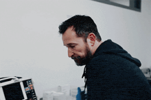 a man in a black hoodie sits in front of a monitor that says ' ecg ' on the screen