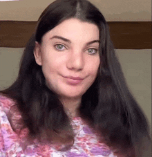 a woman with long black hair and green eyes is wearing a pink and white floral shirt