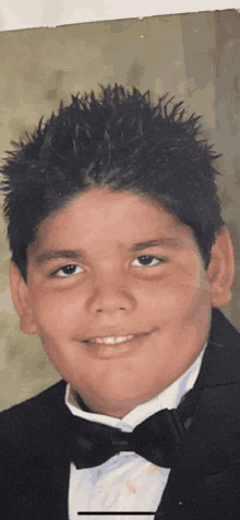 a young boy wearing a tuxedo and bow tie smiles