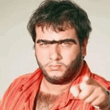 a man with a beard and eyebrows is pointing at the camera with his finger .