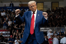 a man in a blue suit and red tie holds his fist up in the air