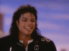 a close up of a man with curly hair smiling in front of a blue sky .