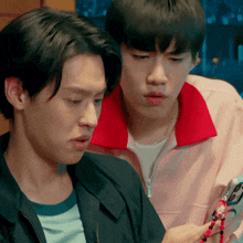 a man in a pink jacket is looking at another man 's necklace