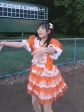 a girl in an orange dress is dancing in front of a scoreboard that says twenty eight