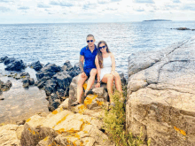 a man and a woman sitting on a rock near the ocean