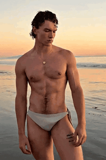 a shirtless man in white swim trunks is standing on the beach
