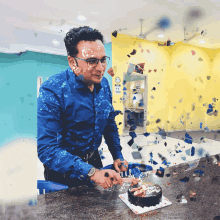 a man in a blue shirt is cutting a cake in front of a no smoking sign