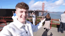 a man in a white jacket with the letter s on it stands in front of the golden gate bridge