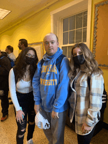 a man wearing a blue sweatshirt with the word university on it poses with two girls