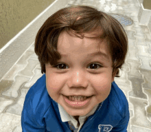 a young boy wearing a blue jacket with the letter d on it smiles for the camera