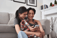 two women are sitting on the floor looking at a cell phone