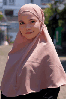 a woman wearing a pink hijab and a black shirt smiles for the camera