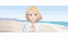 a girl with blonde hair is standing on a beach with her hands folded in front of her chest .