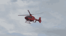 a red helicopter is flying in the sky with a cloudy sky in the background