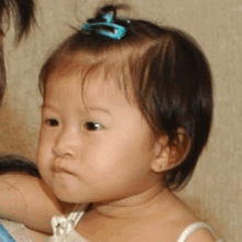 a baby girl with a blue bow in her hair is looking at the camera .