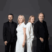 a group of four people standing next to each other in front of a gray background