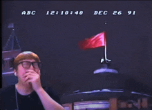 a man wearing glasses is covering his mouth in front of a screen that says abc