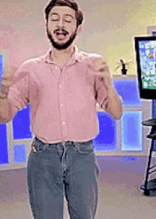 a man in a pink shirt and jeans is standing in front of a tv