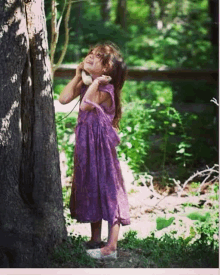 a little girl in a purple dress is talking on a phone