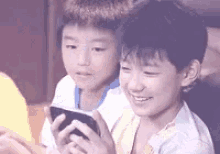 two young boys are playing a game on a cell phone .