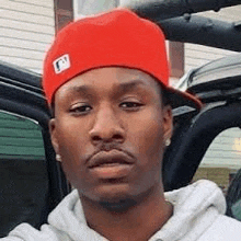 a man wearing a red hat and a white hoodie is taking a selfie in a car .