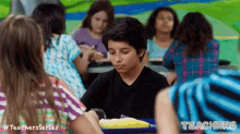 a boy is sitting at a table with a yellow corn on the cob in front of him in a classroom .