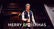 han solo is holding a gun and saying merry christmas while standing in a room .