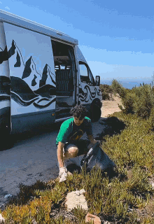 a man in a green shirt is kneeling in front of a white van with mountains painted on the side