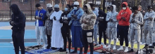 a group of people are standing in a row on a basketball court praying .