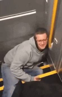 a man in a grey hoodie is holding onto a yellow railing on a set of stairs .