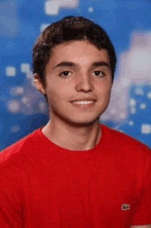 a young man wearing a red t-shirt is smiling for the camera .