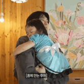 a little girl in a blue dress is being held by a man in front of a painting with flowers