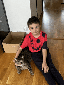 a boy sitting on the floor with a cat wearing a jack o lantern shirt