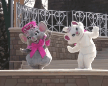 a mouse and a cat mascot are dancing on a stage