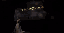 a woman stands in front of a screen that says in memoriam