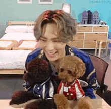 a man is sitting at a table holding two stuffed animals one of which is wearing a red and white shirt