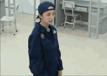 a woman wearing a blue uniform and a blue hat is standing in a room with a desk and chairs